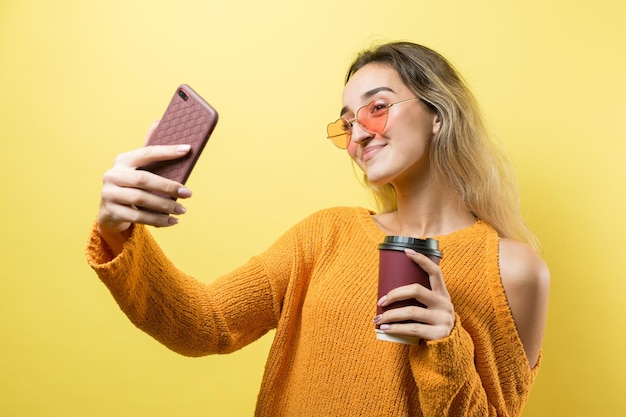 Mujer de glamour en vasos en un suéter naranja con un trago de café sobre un fondo amarillo