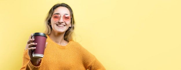 Mujer de glamour en vasos en un suéter naranja con un trago de café sobre un fondo amarillo