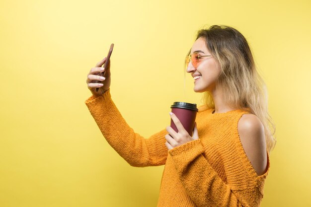 Mujer de glamour en vasos en un suéter naranja con un trago de café sobre un fondo amarillo