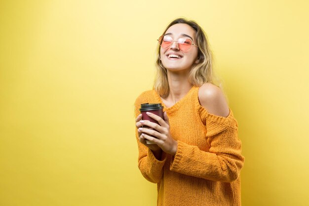 Mujer de glamour en vasos en un suéter naranja con un trago de café sobre un fondo amarillo