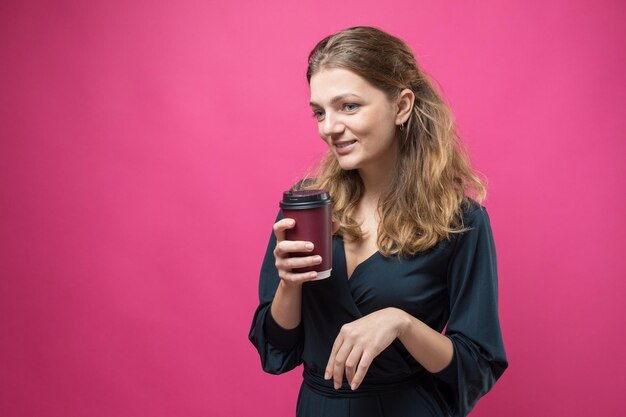 Mujer de glamour en un vestido azul oscuro con un trago de café sobre un fondo rosa