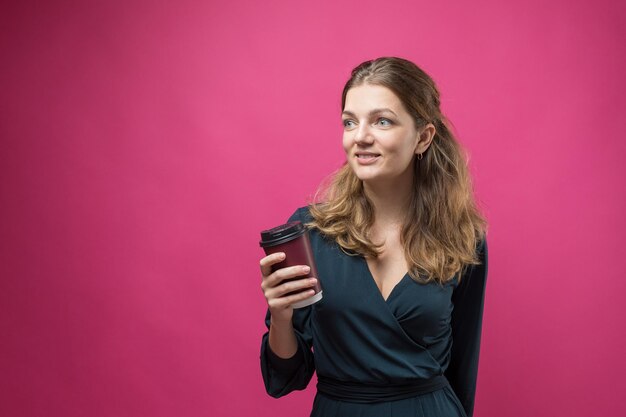 Mujer de glamour en un vestido azul oscuro con un trago de café sobre un fondo rosa