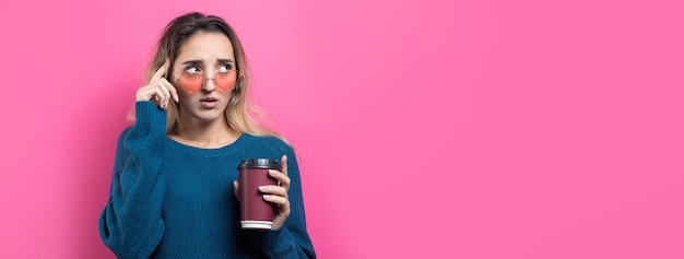 Mujer glamurosa con gafas en un suéter azul con un trago de café en un fondo rosa