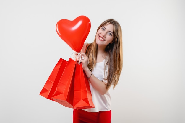 Mujer con globo en forma de corazón rojo y bolsas de compras aisladas