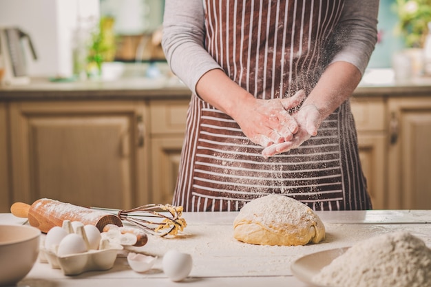 Mujer golpea sus manos por encima de la masa de cerca. Baker termina su panadería, se sacude la harina de las manos, deja espacio libre para el texto. Panadería casera, concepto de proceso de cocción