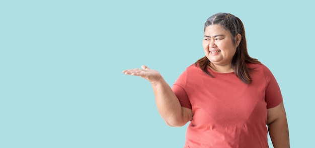 Mujer gorda asiática feliz sonriendo con espacio en blanco de la mano y mostrando aislado sobre fondo azul.