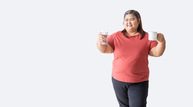 Mujer gorda asiática feliz sonriendo sosteniendo un vaso de agua y taza aislado sobre fondo blanco.