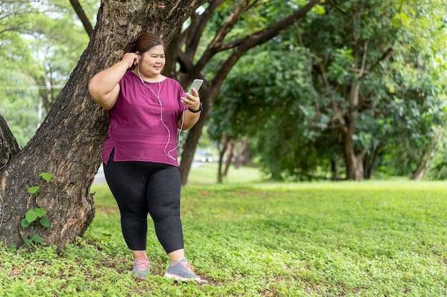 Mujer gorda asiática sosteniendo un teléfono inteligente con escuchar música. Ejercicio al aire libre para el concepto de idea de pérdida de peso