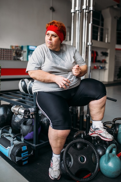 Mujer gorda bebe agua después de entrenar en el gimnasio