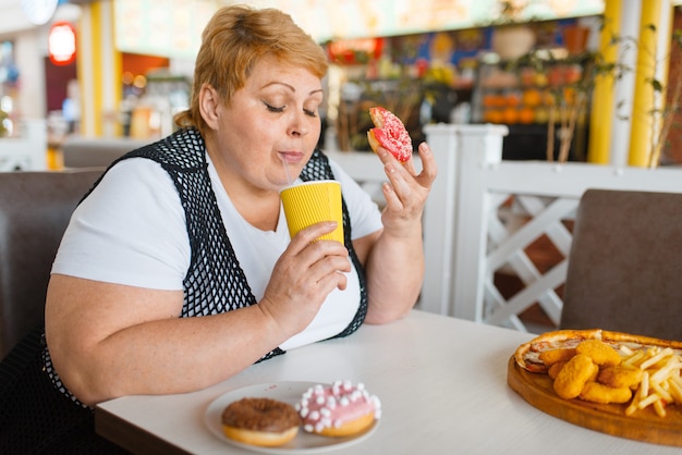 Mujer gorda comiendo donas en restaurante de comida rápida