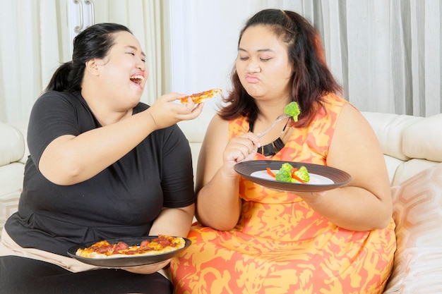 Mujer gorda feliz burlándose de su hermana gorda en dieta