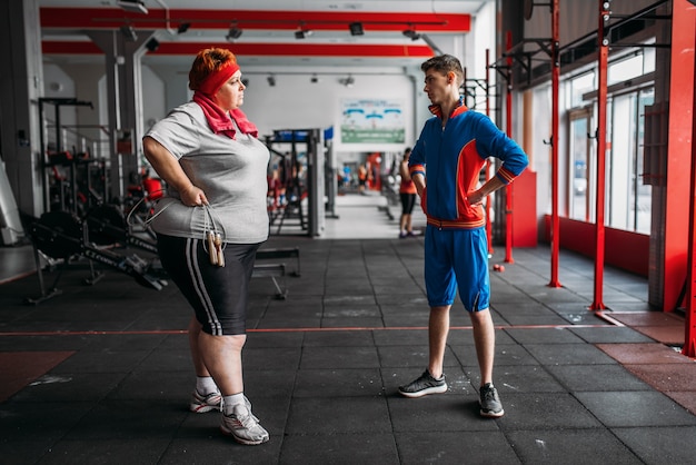 Mujer gorda habla con el instructor después del ejercicio con cuerda en el gimnasio.