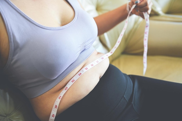 Mujer gorda midiendo mujer gorda vientre gordo gordito panzón deporte recreación cuidado de la salud perder el concepto de grasa del vientre mujer sosteniendo el vientre excesivo con cinta métrica