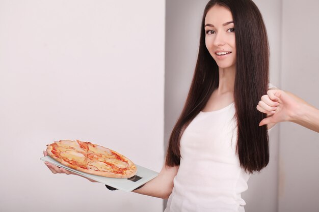 Mujer gorda que se coloca en la balanza que sostiene la pizza.