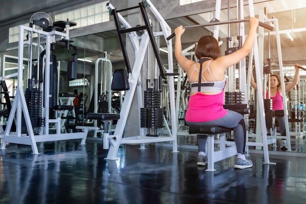 Mujer gorda senior asiática en ropa deportiva entrenando con la máquina en el gimnasio.