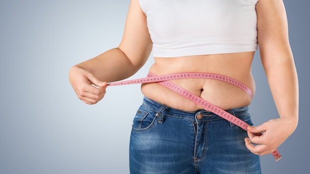 Foto mujer gorda con sobrepeso midiendo su estómago en segundo plano.