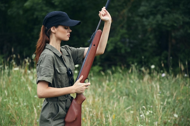 Mujer con gorra negra y un mono verde sostiene un arma en sus manos fondo del bosque