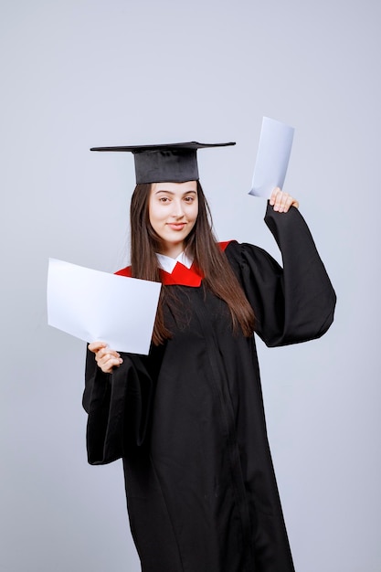 Mujer con gorro de graduación y bata de ceremonia con papeles vacíos. Foto de alta calidad