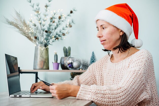 Una mujer con gorro de Papá Noel de compras en línea para regalos de Navidad en su computadora portátil