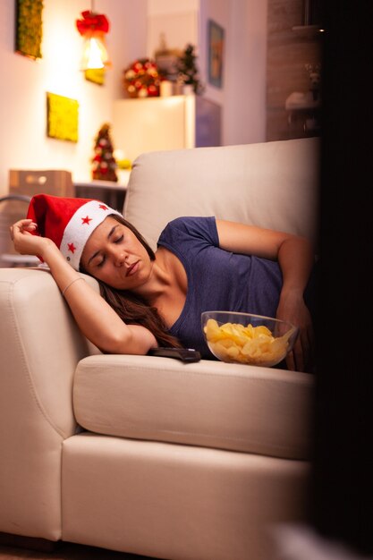 Mujer con gorro de Papá Noel durmiendo en el sofá después de ver una película de entretenimiento de invierno
