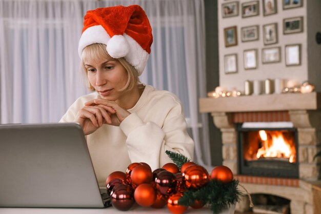 Una mujer con un gorro de Papá Noel felicita a familiares y amigos en una computadora portátil con Navidad Año Nuevo