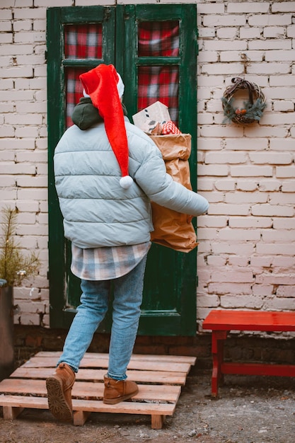 Mujer con gorro de Papá Noel lleva una bolsa de regalos desde la puerta principal del porche de la casa.