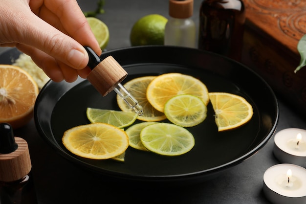 Mujer goteando aceite esencial en un tazón con limones en el primer plano de la mesa gris Tratamiento de aromaterapia