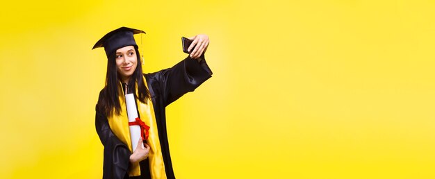 Mujer graduada hace foto selfie sobre espacio amarillo