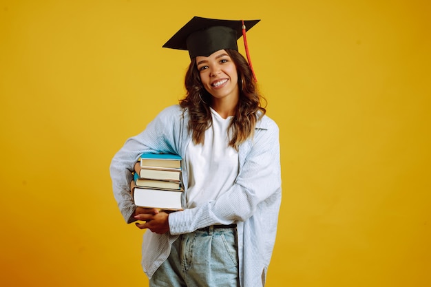 Mujer graduada con un sombrero de graduación en la cabeza, con libros en amarillo.