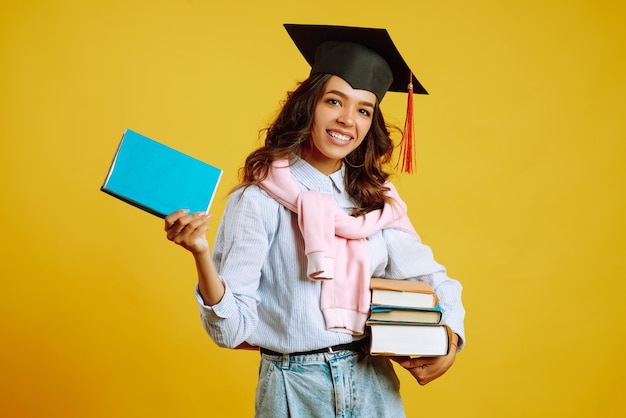 Mujer graduada con un sombrero de graduación en la cabeza, con libros en amarillo.