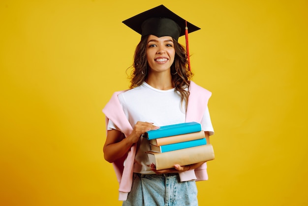 Mujer graduada con un sombrero de graduación en la cabeza, con libros en amarillo.