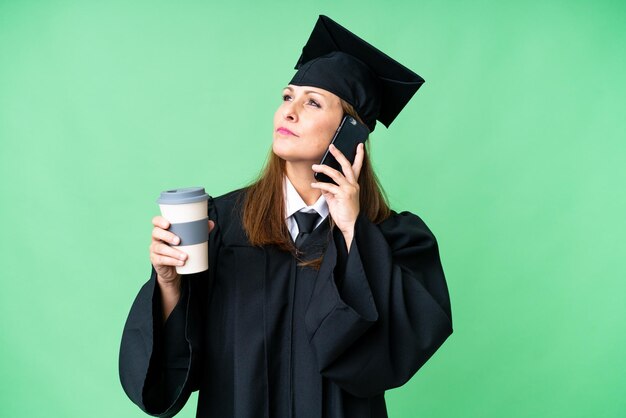 Mujer graduada universitaria de mediana edad sobre antecedentes aislados sosteniendo café para llevar y un móvil