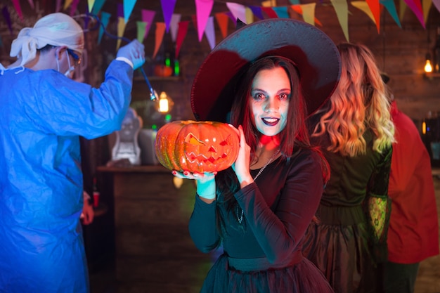 Mujer con una gran sonrisa vestida como una bruja para la celebración de Halloween. Chica sosteniendo una calabaza.