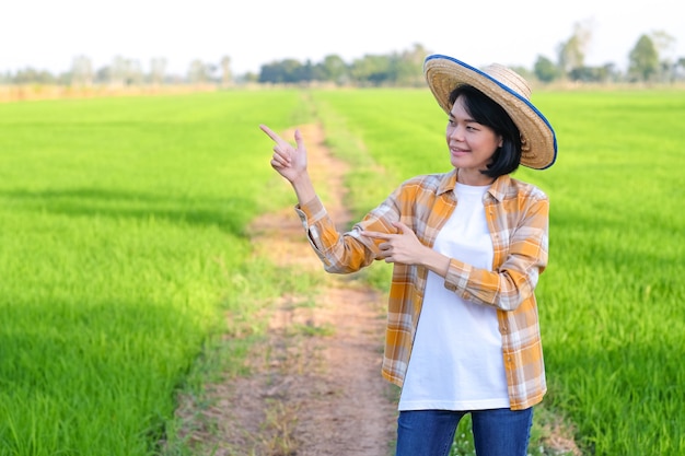 La mujer del granjero asiático levantó las manos apuntando al lado de la imagen con espacio de copia.