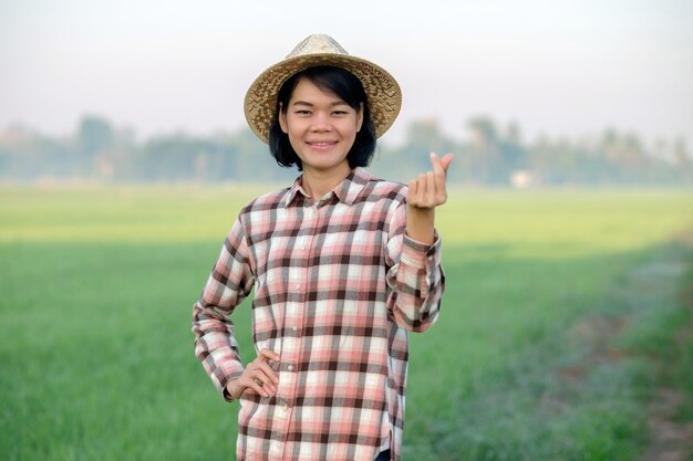 La mujer del granjero asiático sonríe y hace un signo caro con sus dedos en una granja de arroz verde