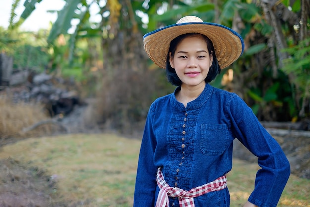 La mujer del granjero asiático usa la sonrisa del traje tradicional azul y de pie en la granja