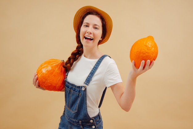 La mujer del granjero feliz en monos muestra la cosecha de otoño fresca de calabazas orgánicas sobre fondo amarillo