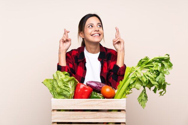 Mujer del granjero que sostiene verduras frescas en una cesta de madera con cruzar los dedos