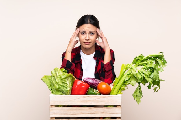 Mujer del granjero que sostiene verduras frescas en una cesta de madera infeliz y frustrada con algo. Expresión facial negativa