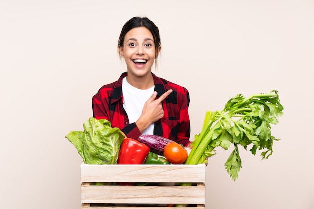 Mujer del granjero que sostiene verduras frescas en una cesta de madera que señala el dedo al lado