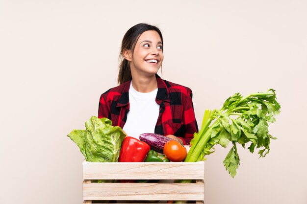 Mujer del granjero que sostiene verduras frescas en una cesta de madera riendo y mirando hacia arriba