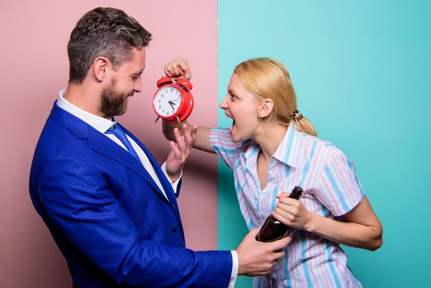 Mujer gritando y enojada muestra la hora en el despertador esposa preguntándose por qué el esposo llegó tan tarde problemas de rutina de pareja familiar en relación psicología familiar vida infeliz hombre bebida alcohólica vino