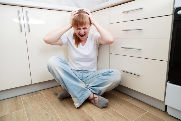 Foto mujer gritando enojada sentada en el suelo en la cocina