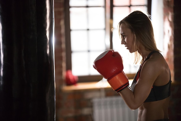 Una mujer con guantes de boxeadores de pie en el gimnasio.