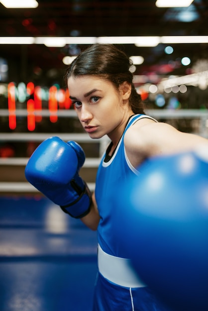 Mujer con guantes de boxeo azules golpea, box training en ring. Boxeadora en el gimnasio, entrenamiento de kickboxing en el club deportivo, entrenamiento de kickboxer de niña