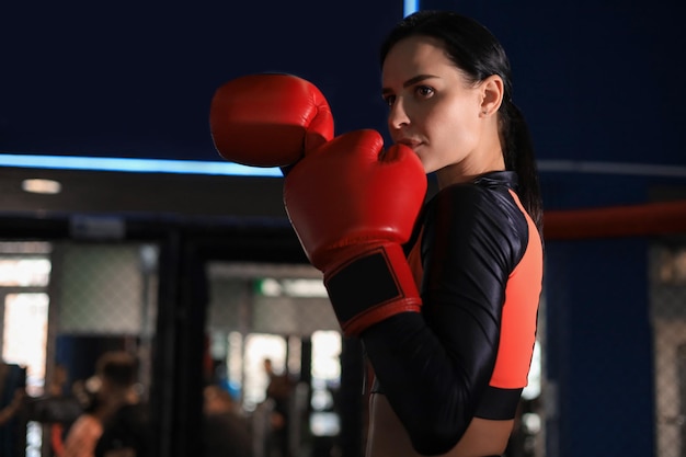 Foto mujer con guantes de boxeo rojos y ropa deportiva se para en un estante en la sala de boxeo