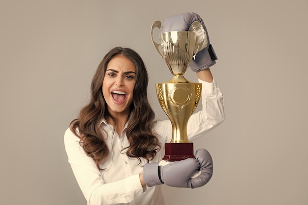 Mujer en guantes de boxeo sostenga el trofeo de la copa ganadora del campeón Gritando fuerte joven boxeadora Fuerte