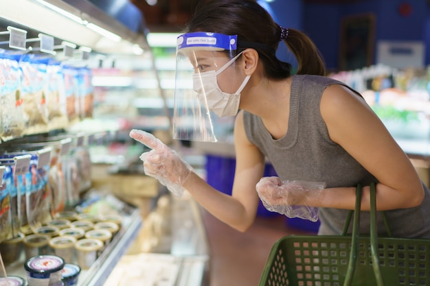 Mujer con guantes, careta y máscara elegir verduras. Compras de pánico durante la pandemia del virus corona.