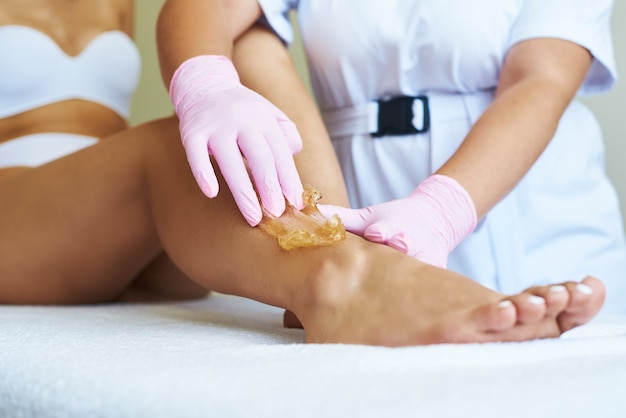 Mujer con guantes de color rosa aplicando crema depilatoria en una pierna