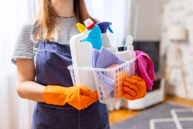 Mujer con guantes de goma con una canasta de suministros de limpieza lista para limpiar